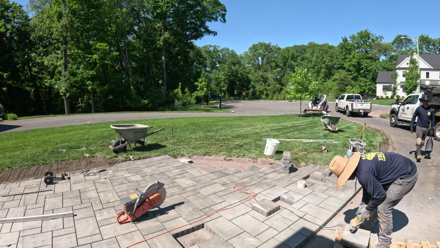Masonry saw cut-block paver installation with rotating crew members working on gray paver patio
