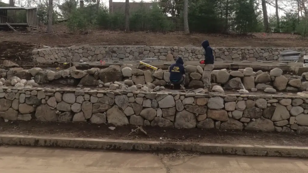 Fieldstone wall build in progress with workers, MA backyard