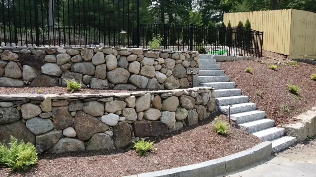 Two-tier fieldstone wall with steps and iron fence, MA