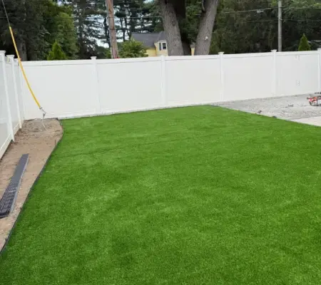 Artificial turf installation Massachusetts backyard white fence low maintenance lawn