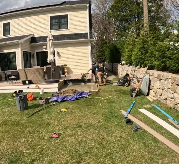 Crew installing natural stone retaining wall and patio base preparation at Lexington Massachusetts home