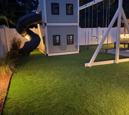 Gray two-story play cottage with tube slide, blue-hour outdoor lighting, Quincy MA