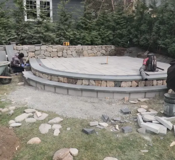 Crew building curved natural stone retaining wall with patio foundation at Massachusetts home