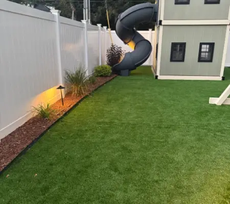 Turf play yard with spiral slide and path lights after dark, Medford MA