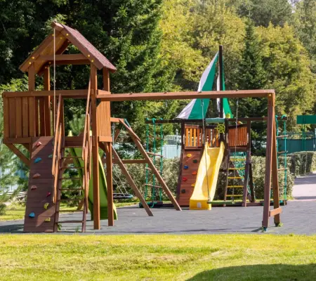 Two-tower wooden playground with climbing wall and yellow slide, fenced community play area, Revere MA